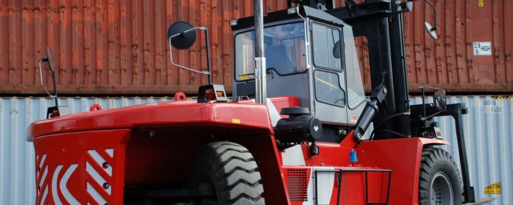 Large red forklift operating among shipping containers at a UK logistics site, supporting bulk materials handling and lifting operations.